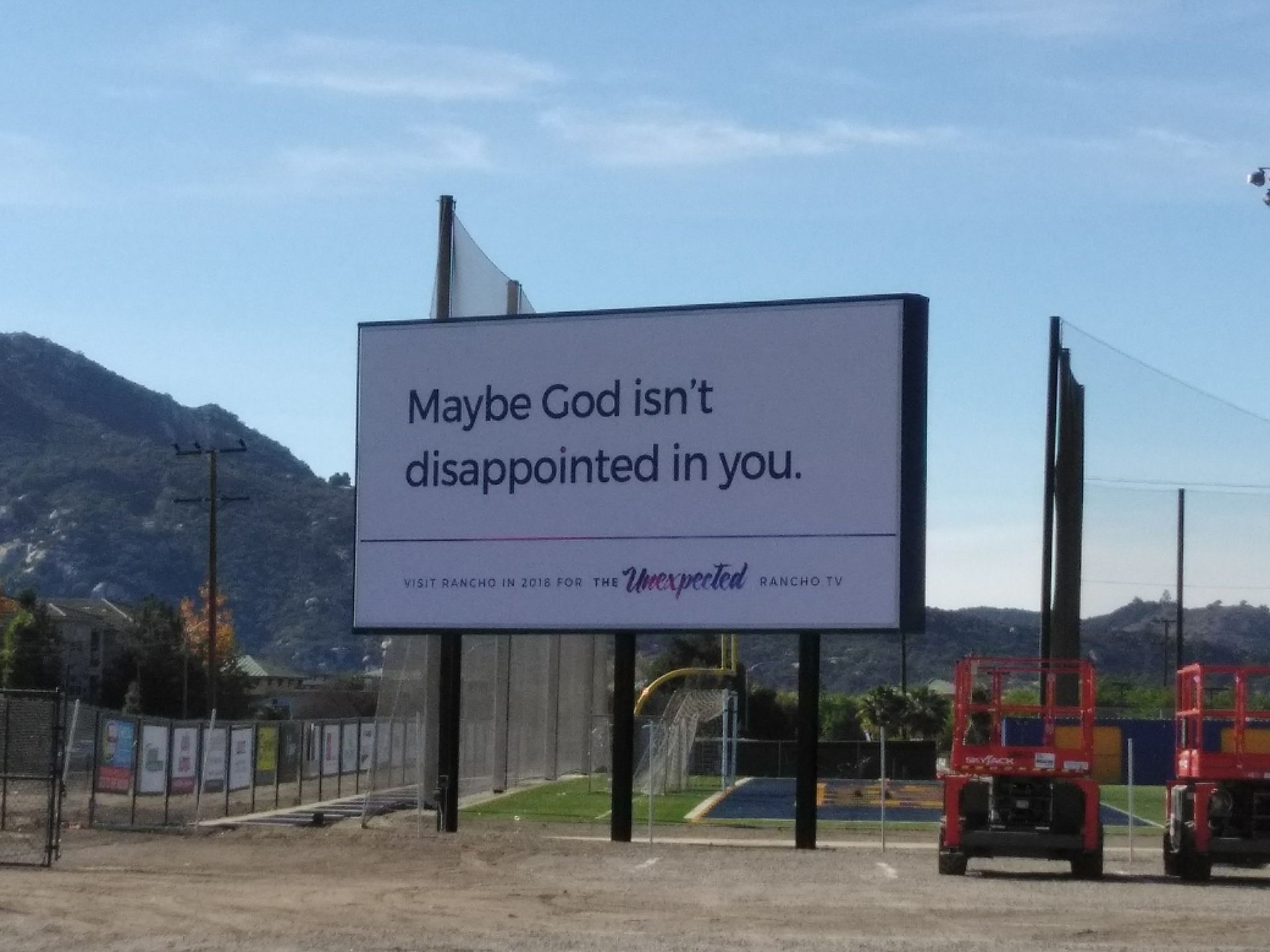 Billboard reading “Maybe God isn’t disappointed in you” on a roadside near mountains