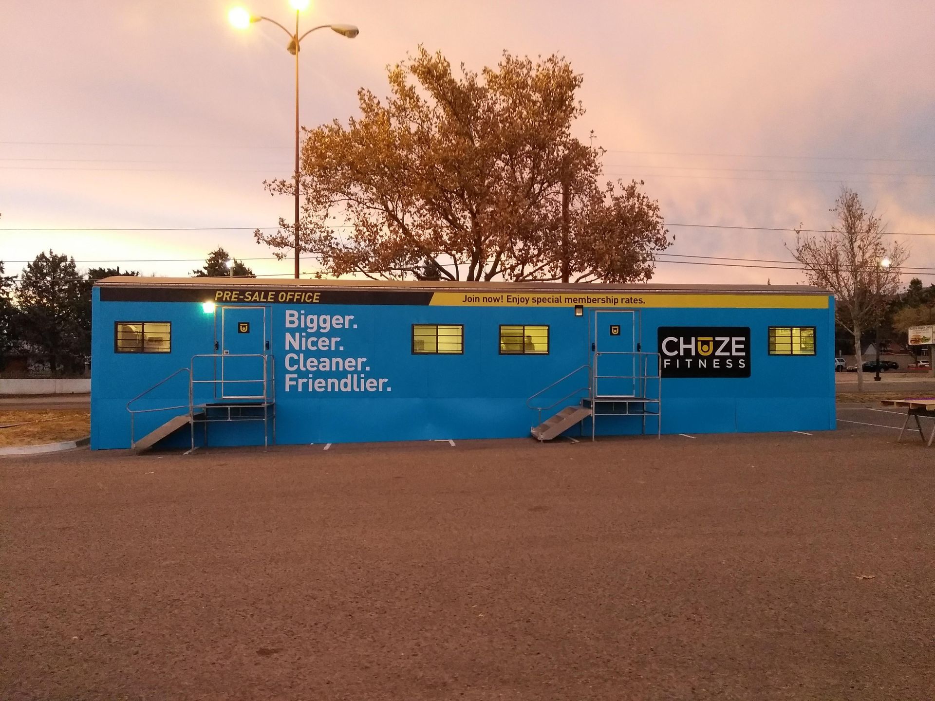 Blue CHAZE food truck at dusk with “Bigger, Nicer, Cleaner, Friendlier” text and trees behind
