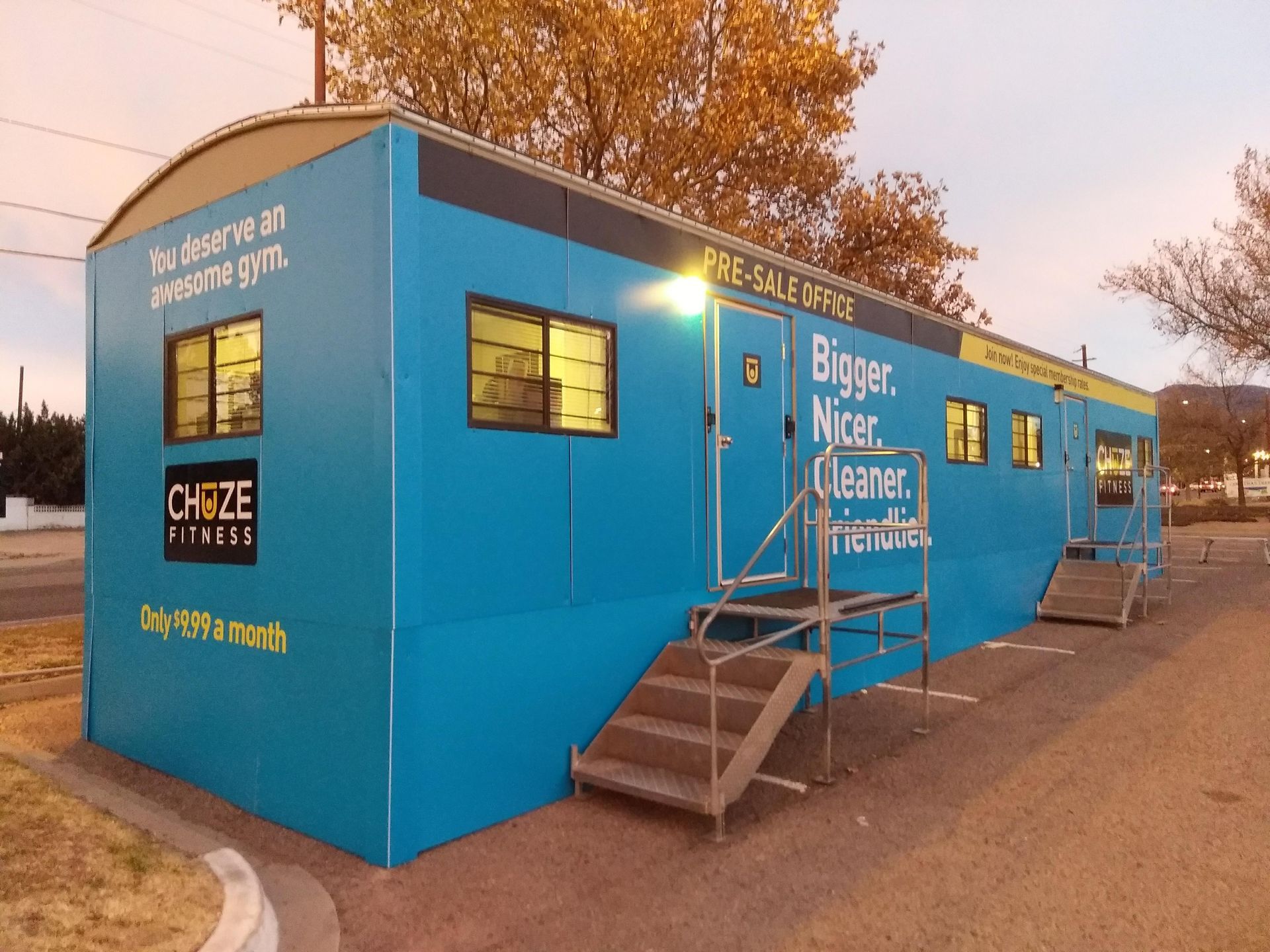 Blue mobile office trailer with steps and “Bigger, better” signage at dusk