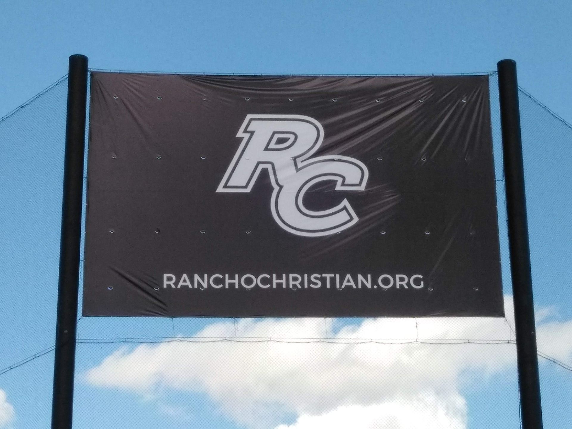 Rancho Christian banner with “RC” logo and ranchochristian.org on a fence against a blue sky