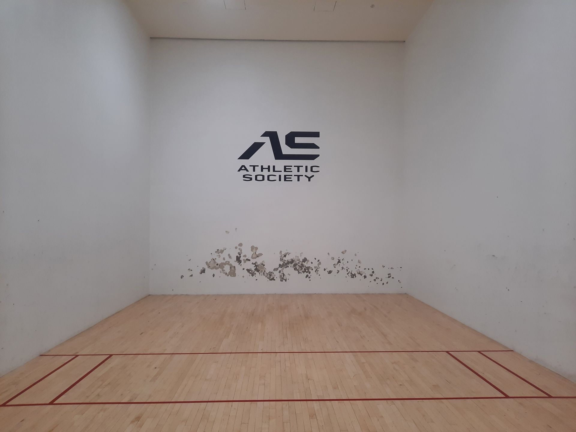 Empty indoor racquetball court with white walls, wood floor, and an 
