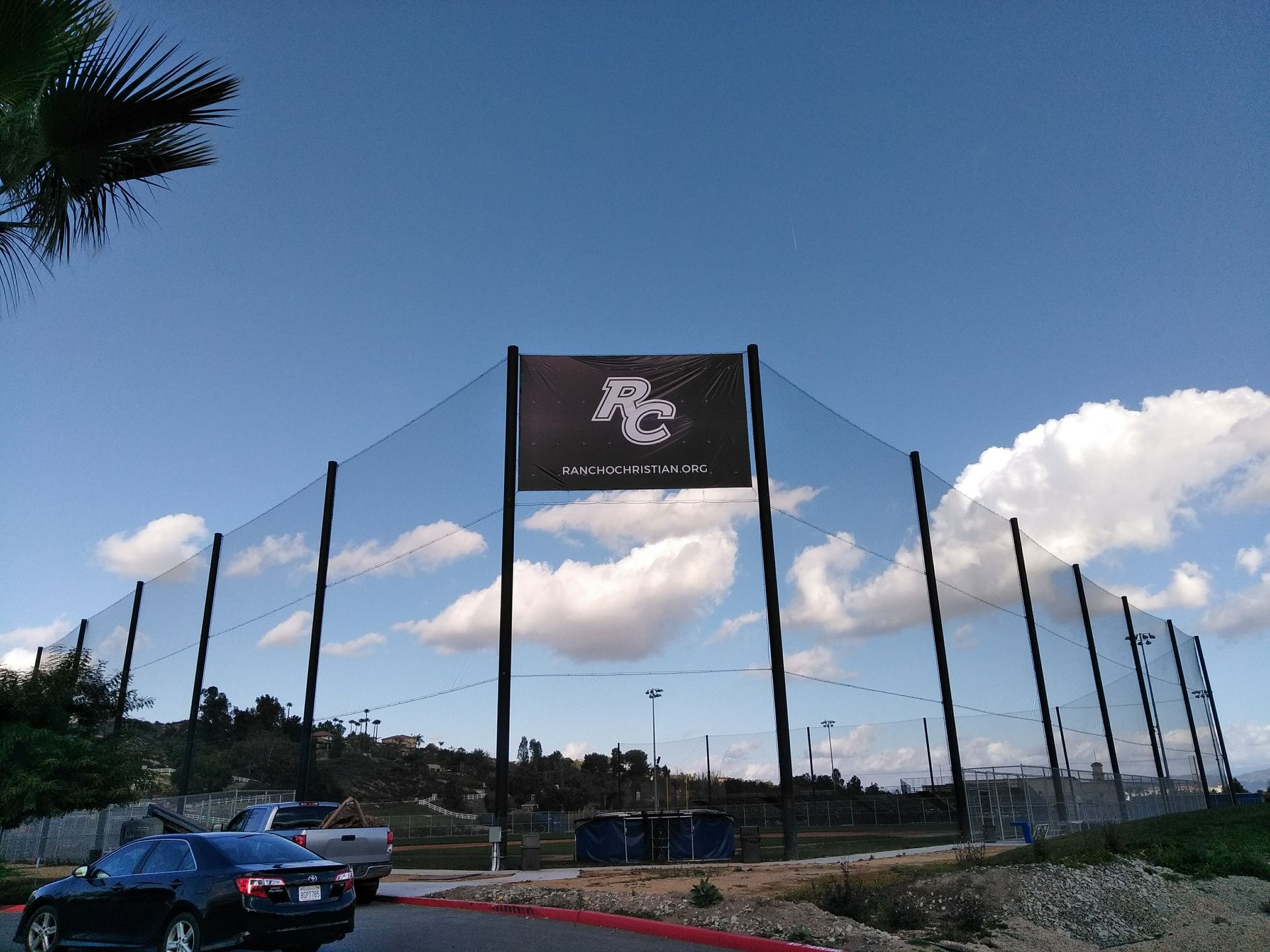 Large sign with a white logo above a roadway, flanked by tall poles under a blue sky with clouds.