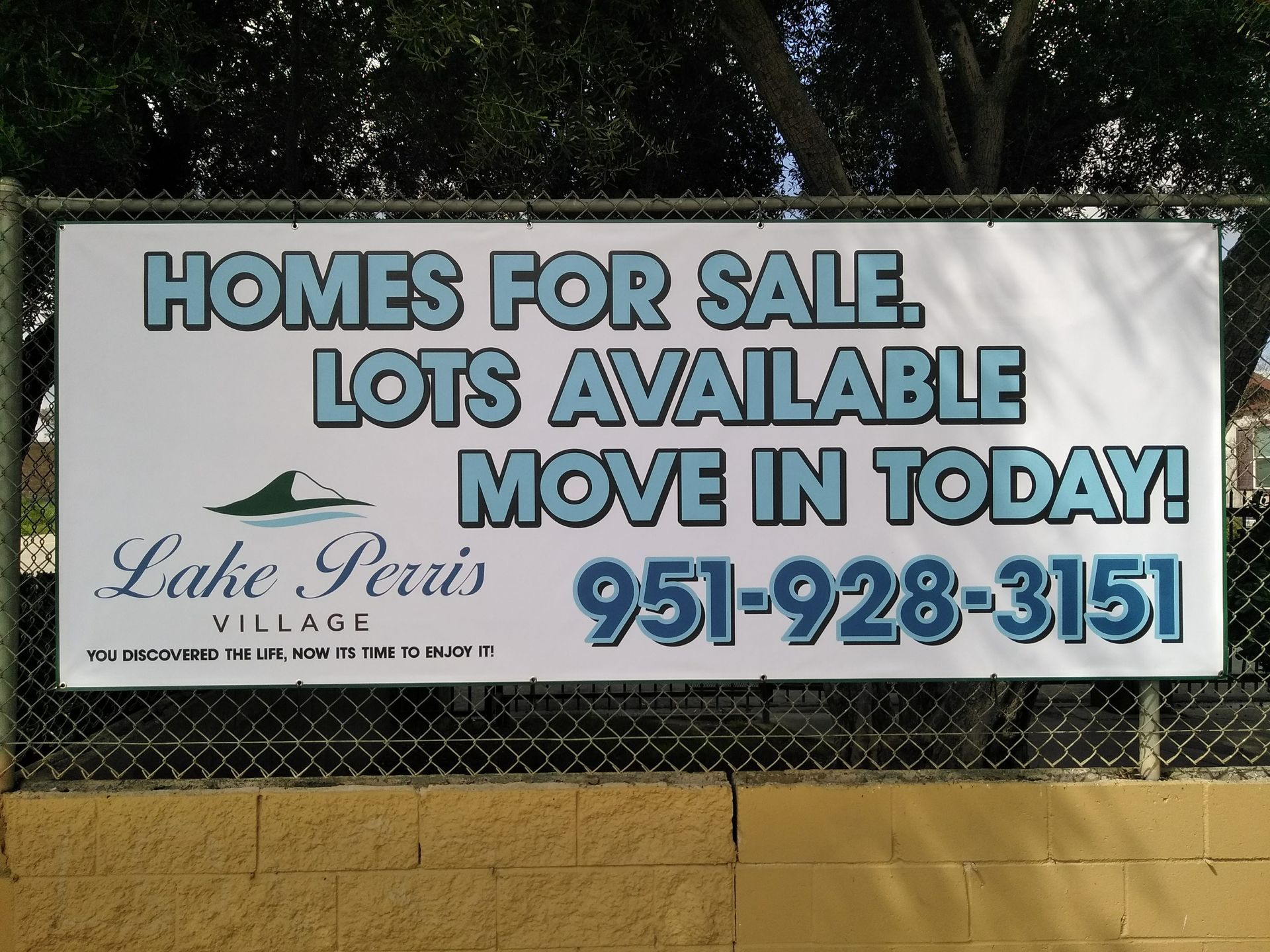 “Homes for Sale” roadside sign with lot availability and phone number 951-928-3151 on a chain-link fence