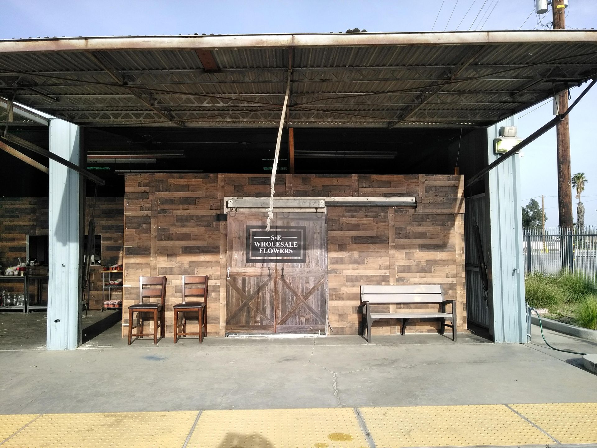 Bus stop shelter with wooden benches and chairs, brick back wall, and a yellow tactile paving strip in front