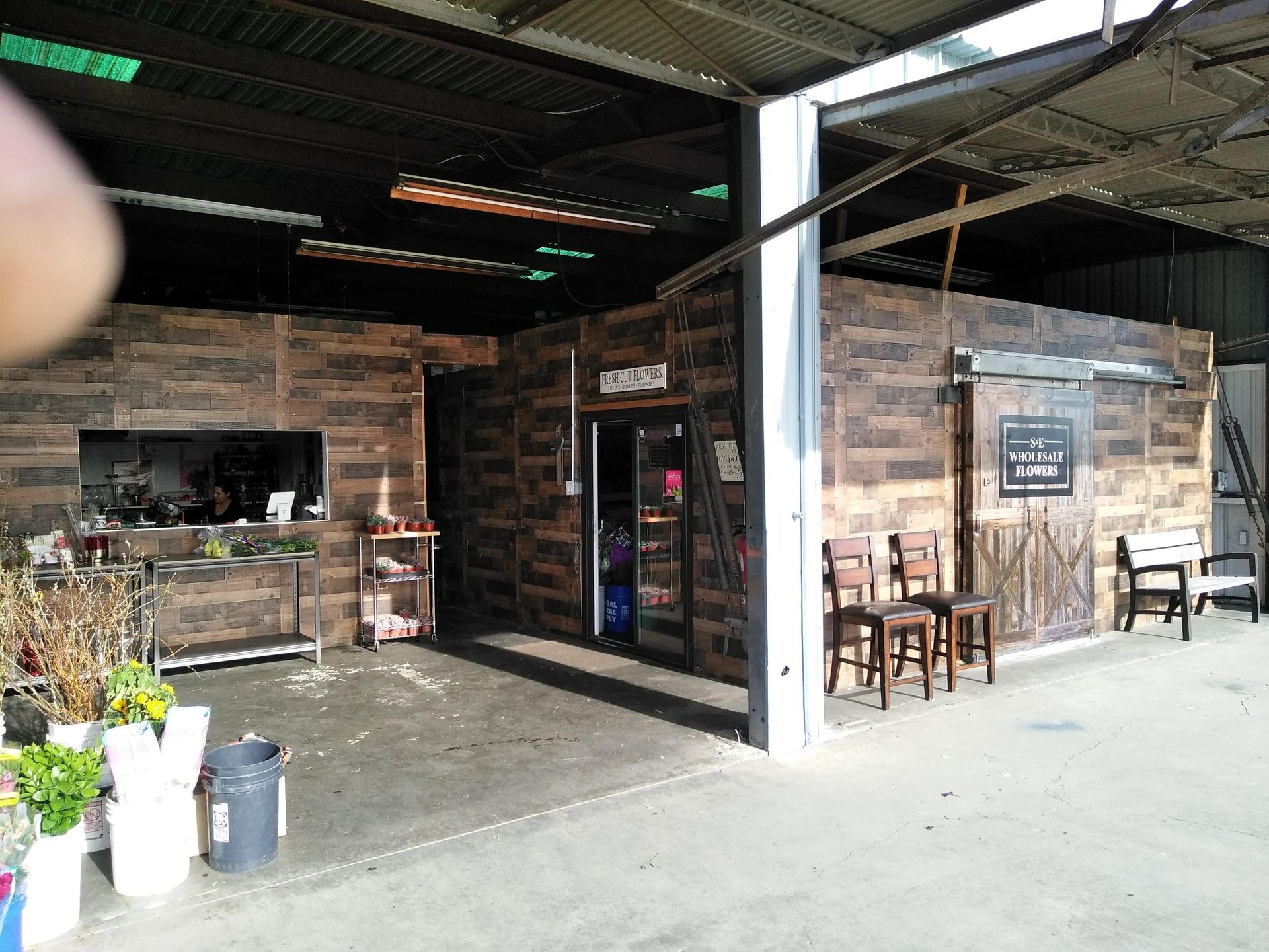 Covered outdoor café entrance with brick walls, tables, and chairs under a metal roof