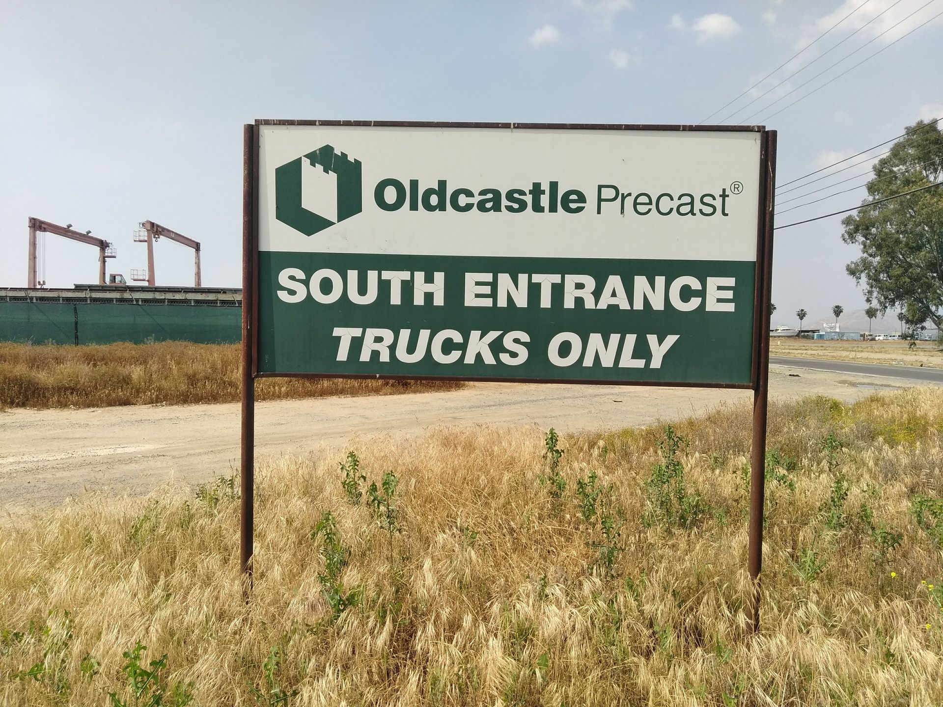 Oldcastle Precast sign reading “South Entrance Trucks Only” beside a road and dry grass.