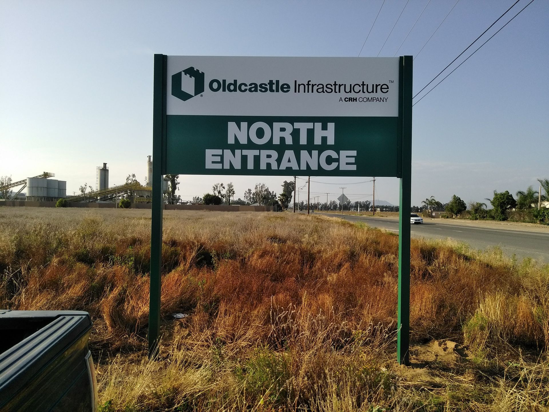 Oldcastle Infrastructure sign reading “NORTH ENTRANCE” beside a roadside field