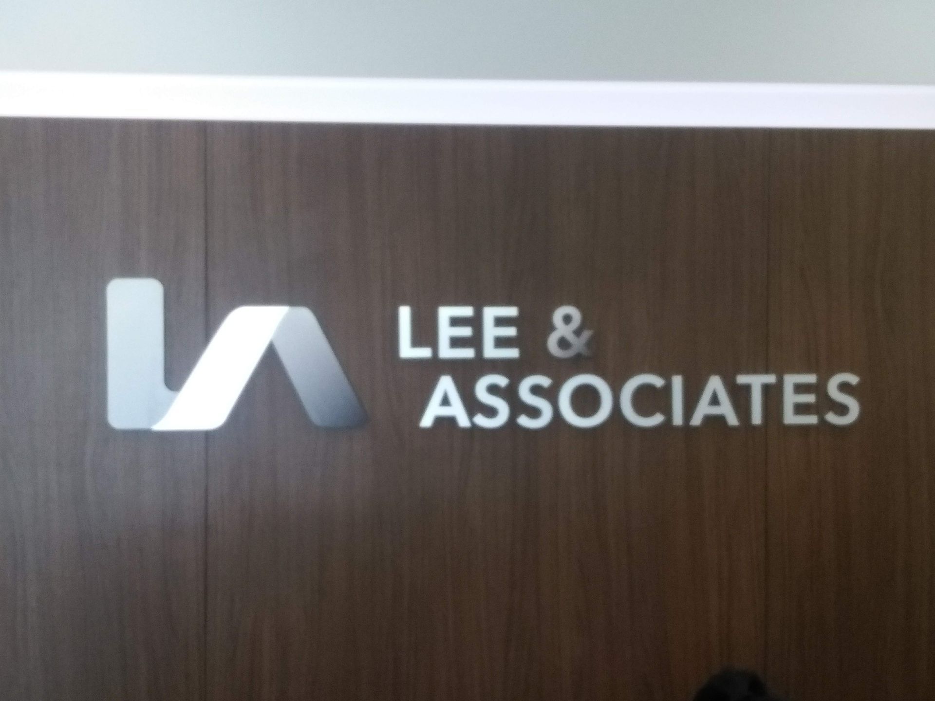 LEE & ASSOCIATES logo on a dark wood wall with a silver emblem