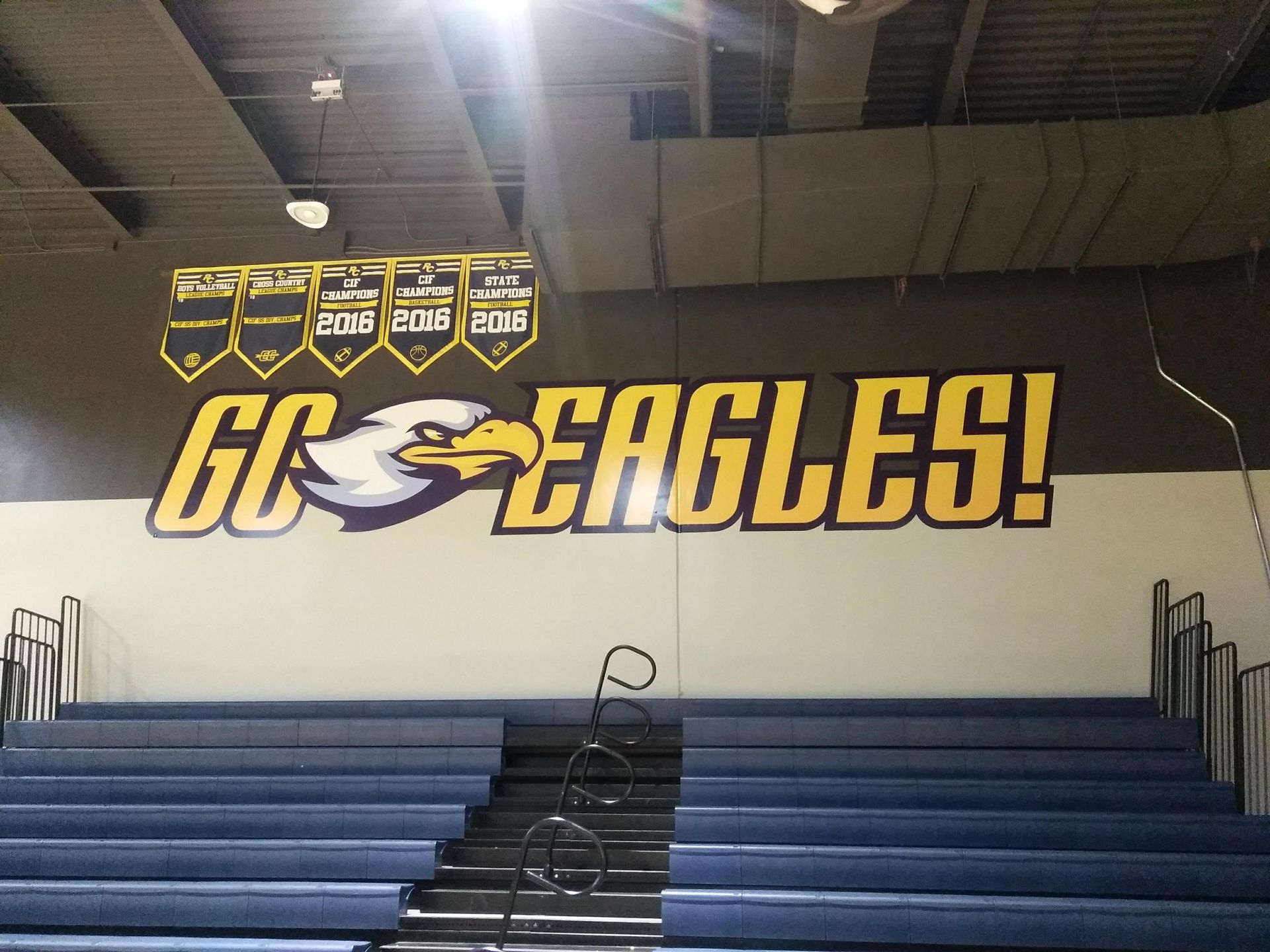 Gym bleachers facing a wall mural reading “GO EAGLES!” in blue and gold.