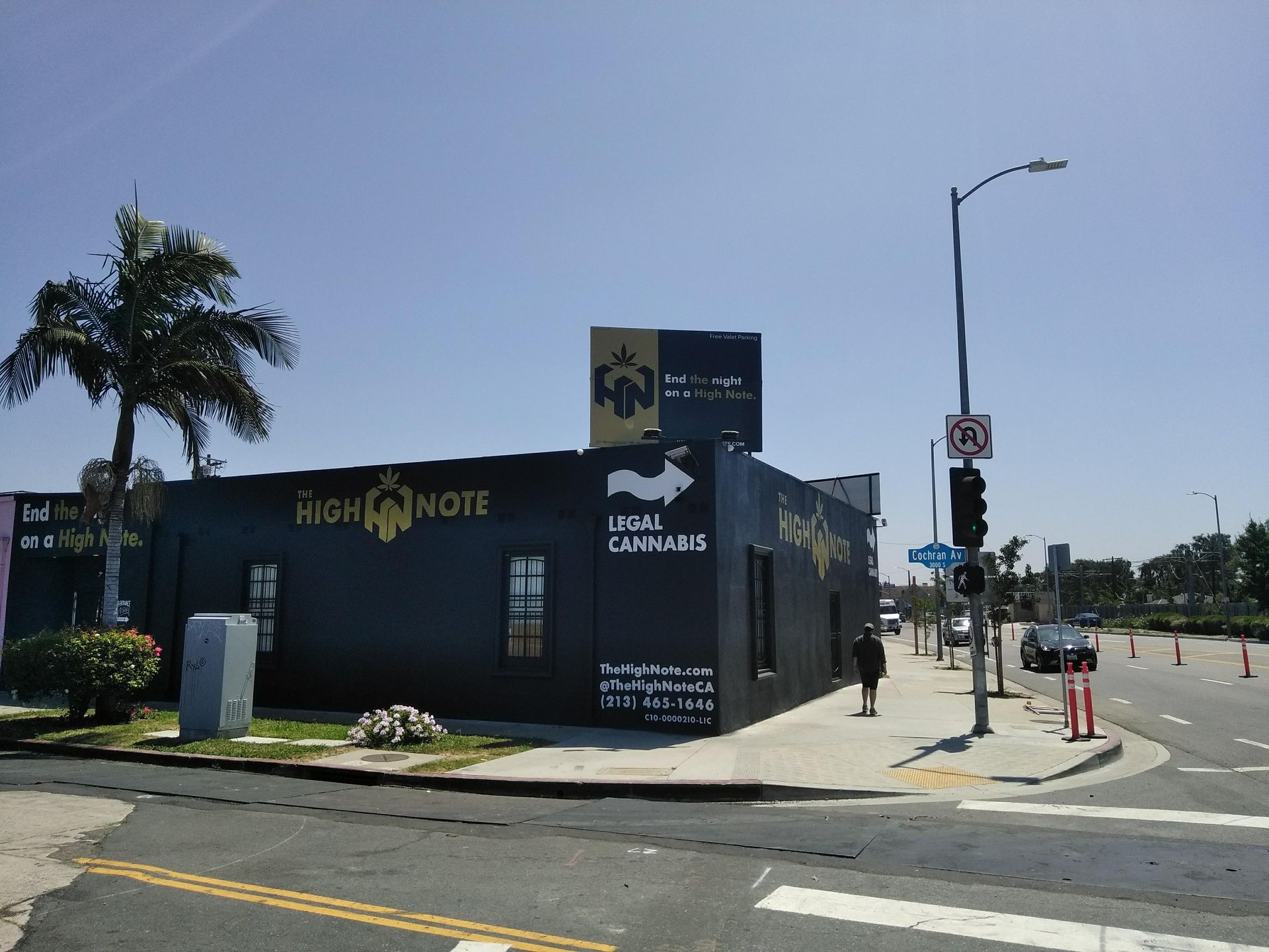 Black building on a sunny street corner with HIGH NOTE signage and palm trees nearby