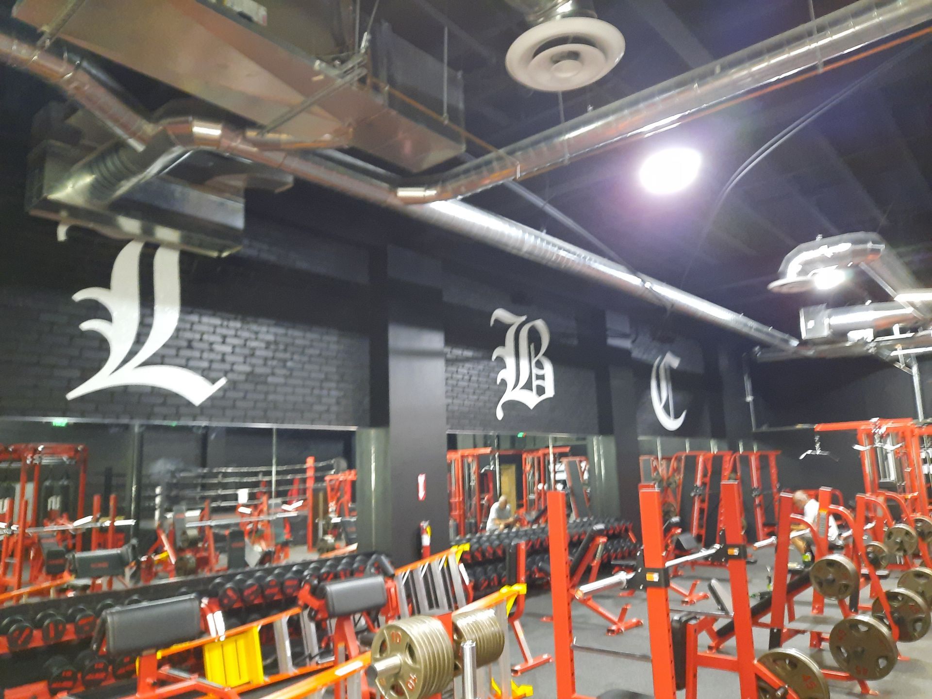 Empty gym with red weight machines and large white letters on black walls and ceiling pipes