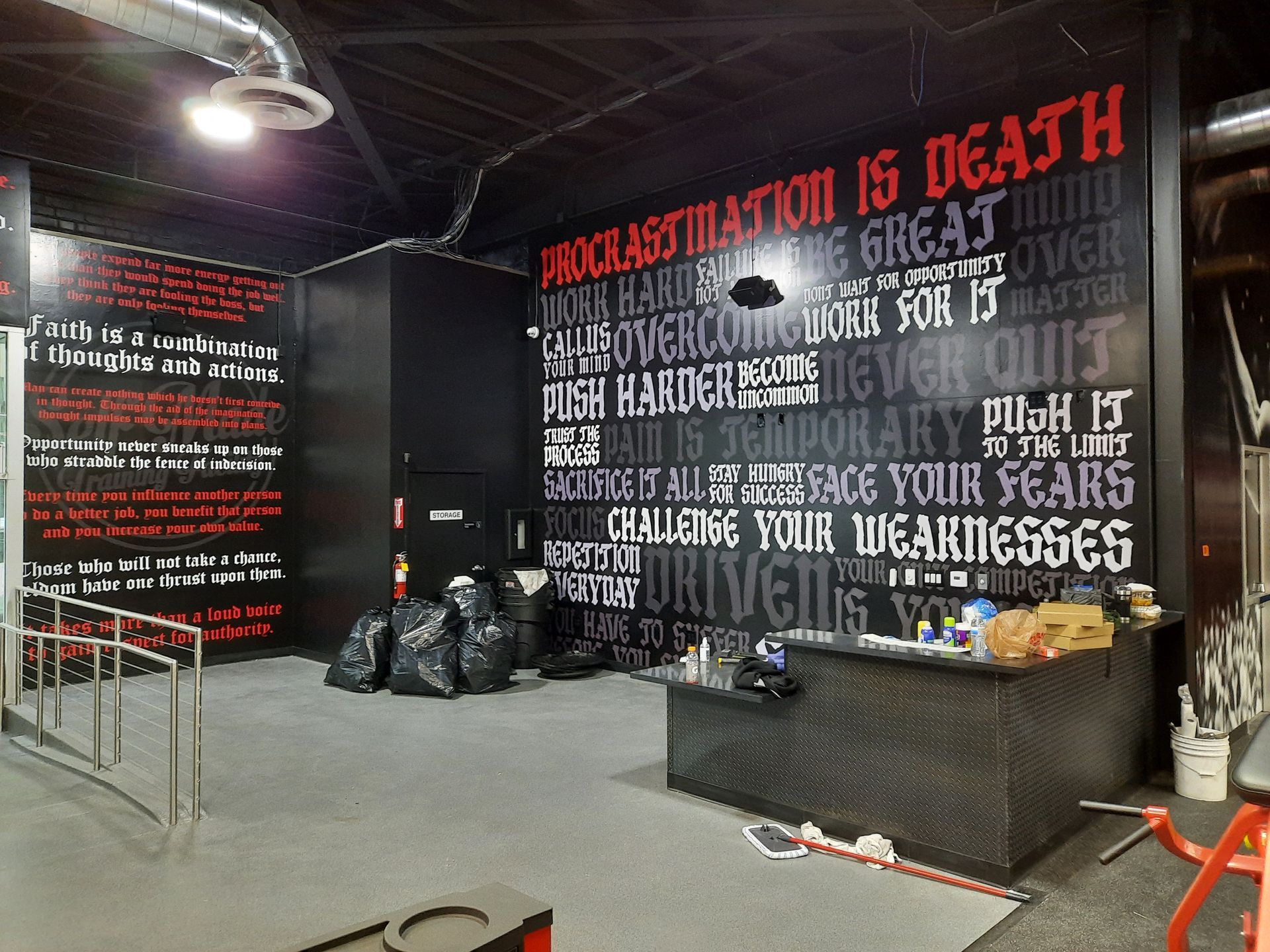 Graffiti-covered wall in an industrial interior with a long black bench and trash bags nearby