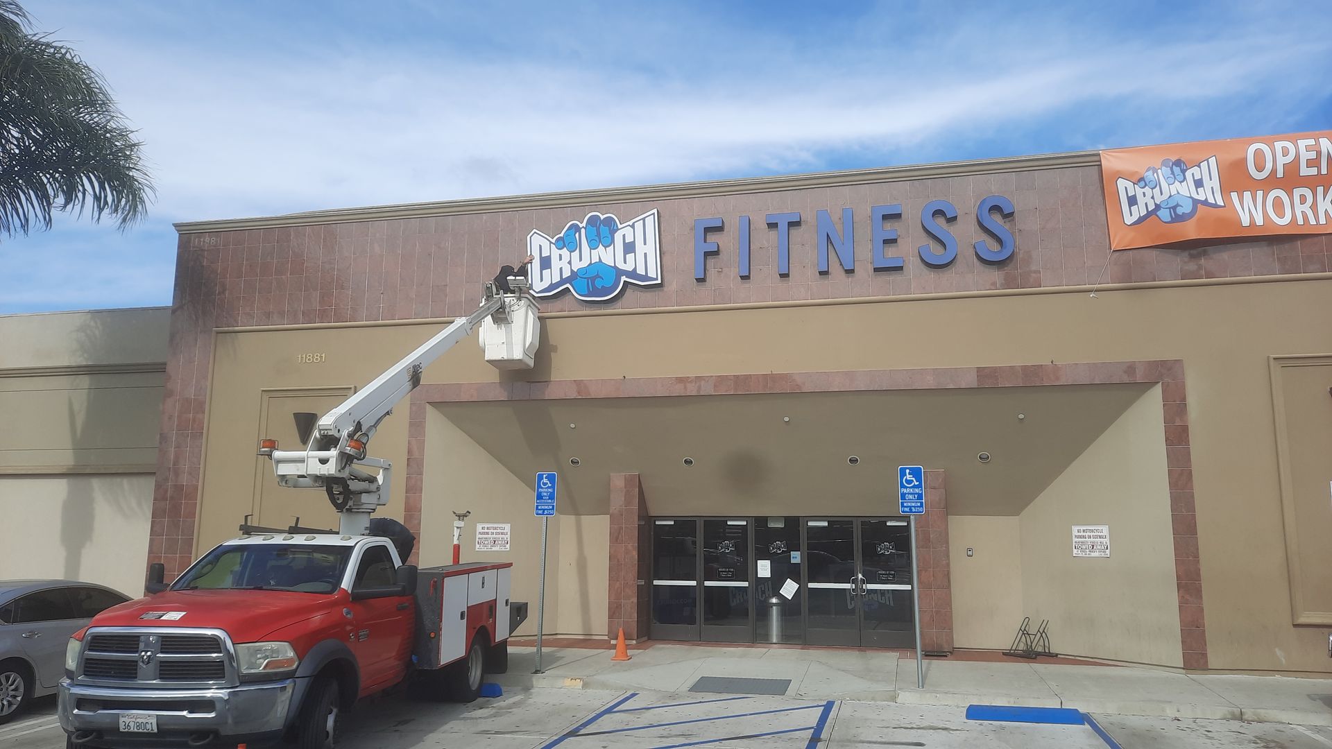Fitness storefront with a worker in a lift truck installing a sign above the entrance