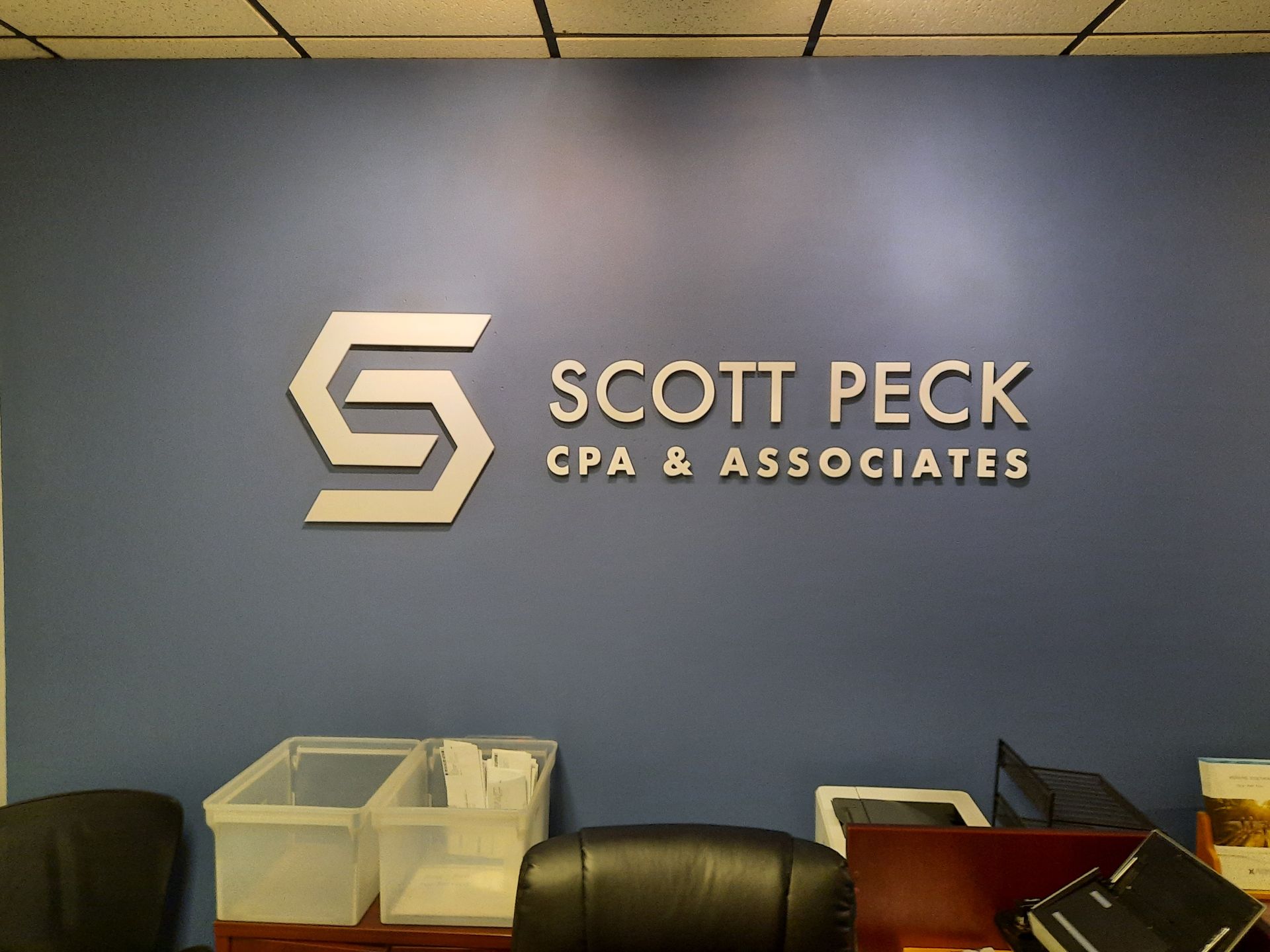 Scott Peck CPA & Associates logo on a blue office wall above chairs and storage bins