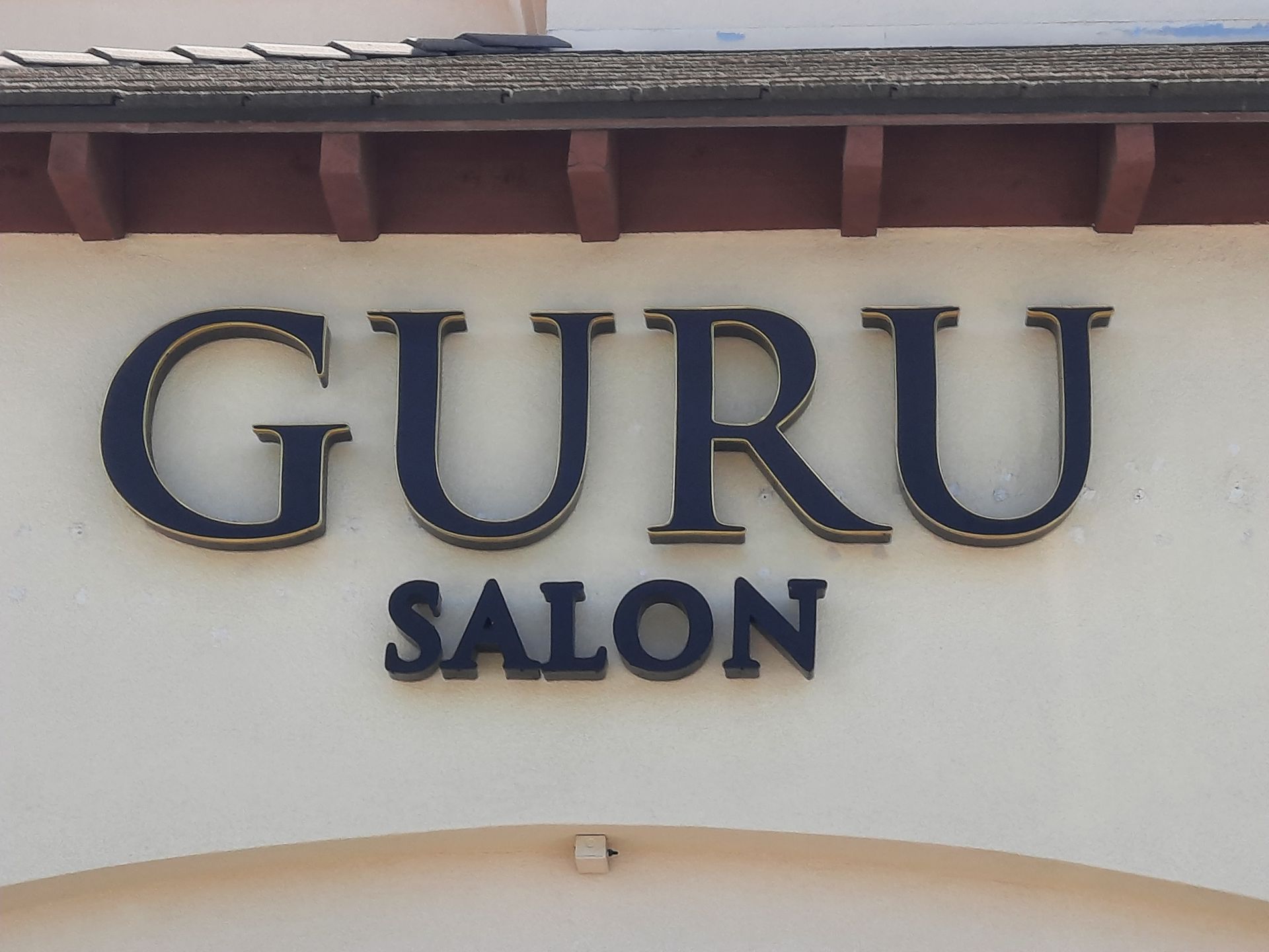GURU SALON sign in dark blue letters on a light wall under a roof overhang