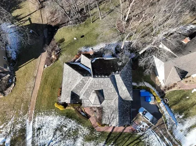 Aerial view of a house with a gray roof and brick pathway, surrounded by grass and snow-covered ground.