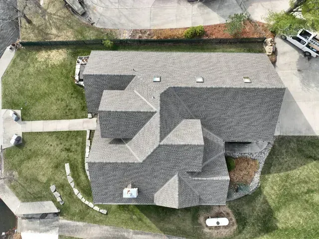 Overhead view of a house with a gray roof, surrounded by green grass and a concrete driveway.
