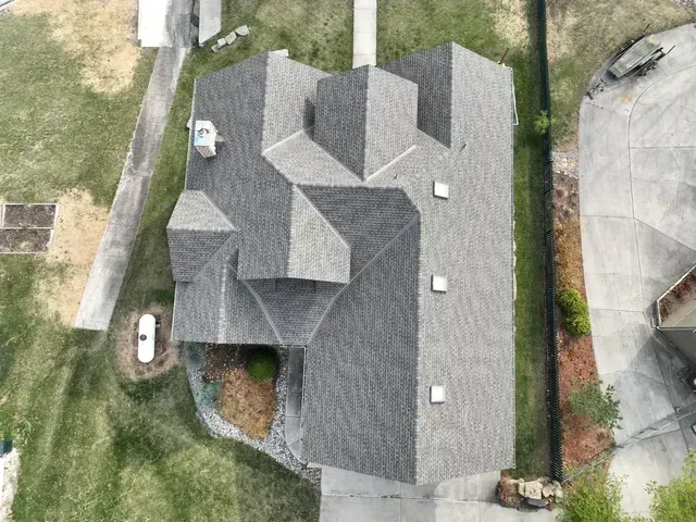 Overhead view of a house with a gray roof, surrounded by green grass and a concrete driveway.