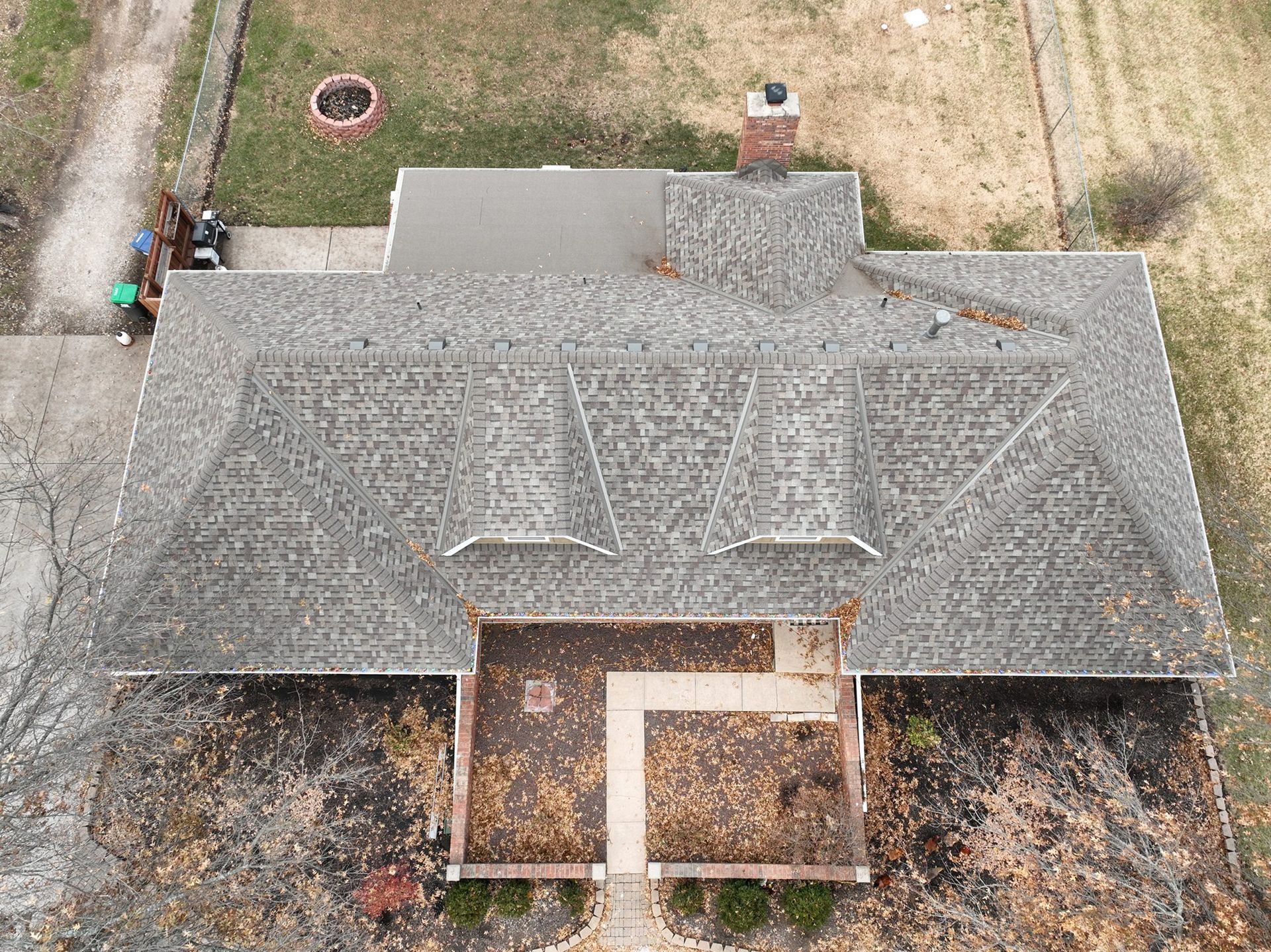 Overhead view of a house with a gray shingled roof, chimney, and patio covered in fall leaves.