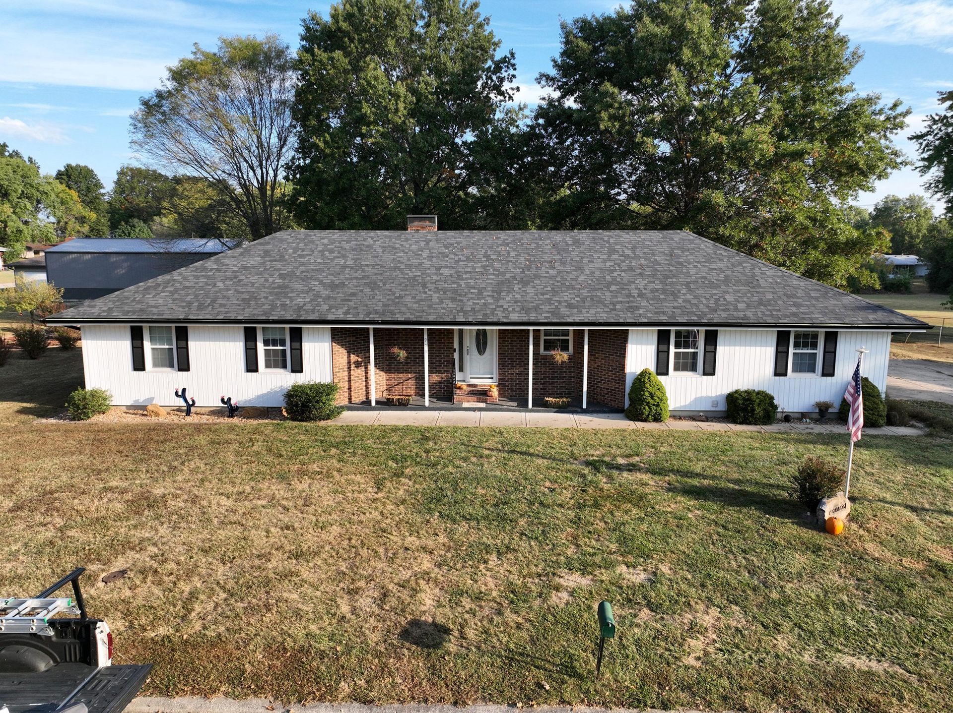 White house with dark gray roof and shutters, brown brick accents, and green lawn.