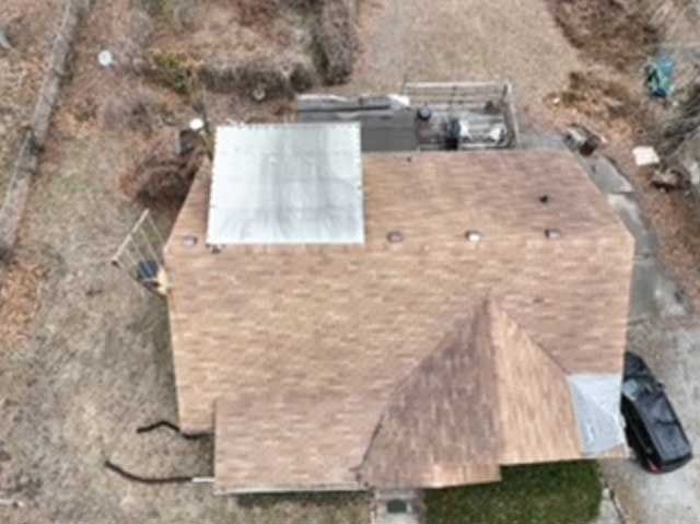 Overhead view of a house with a brown shingled roof, a rectangular silver section, and a black car.