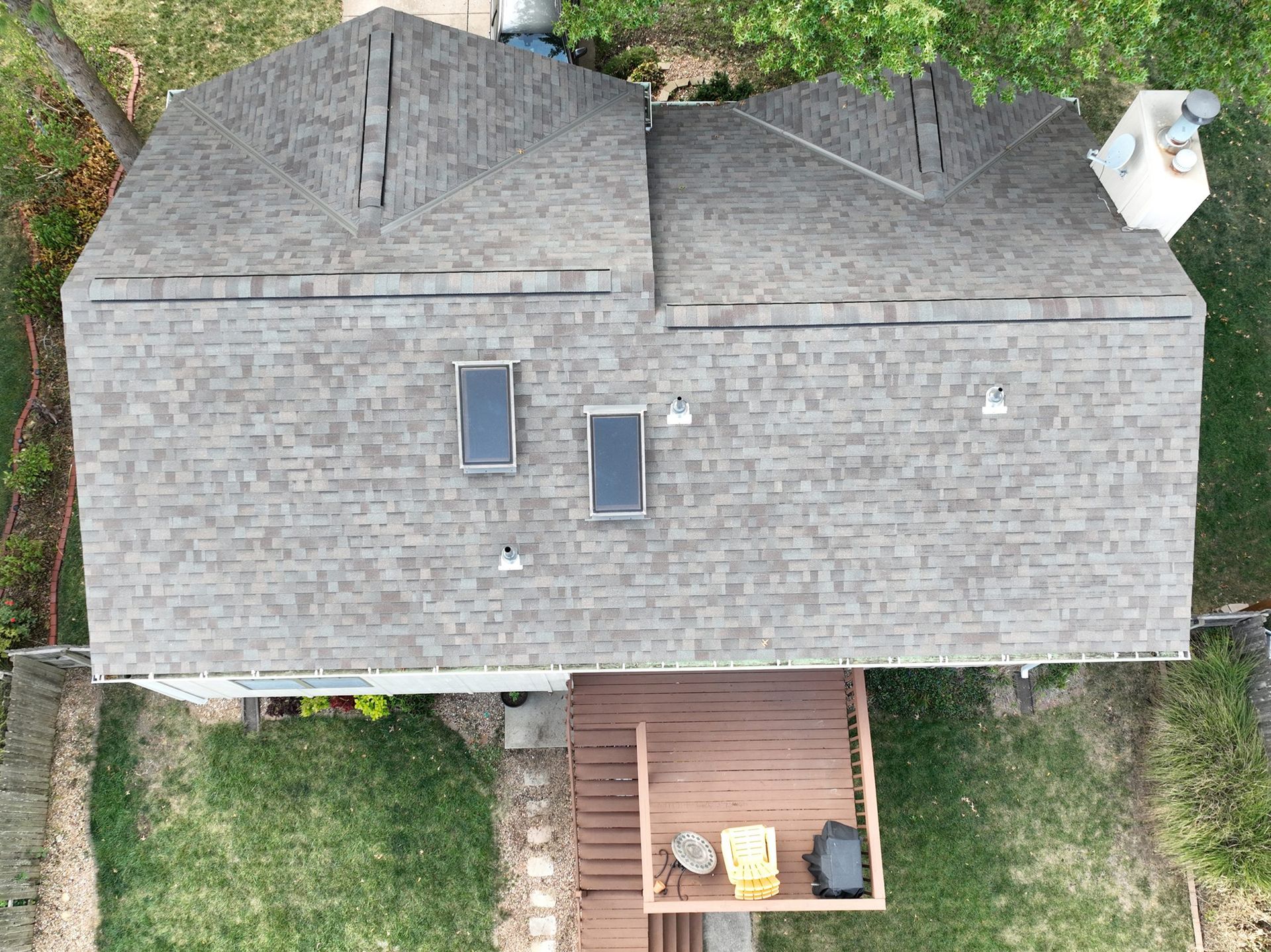 Overhead view of a house with a brown shingled roof, skylights, and a wooden deck.
