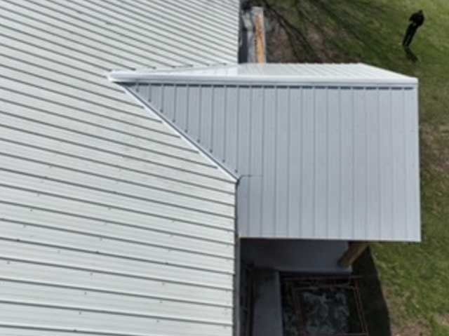 White metal roof on a building, with a lower roof section on the right, and a person walking in the grass.