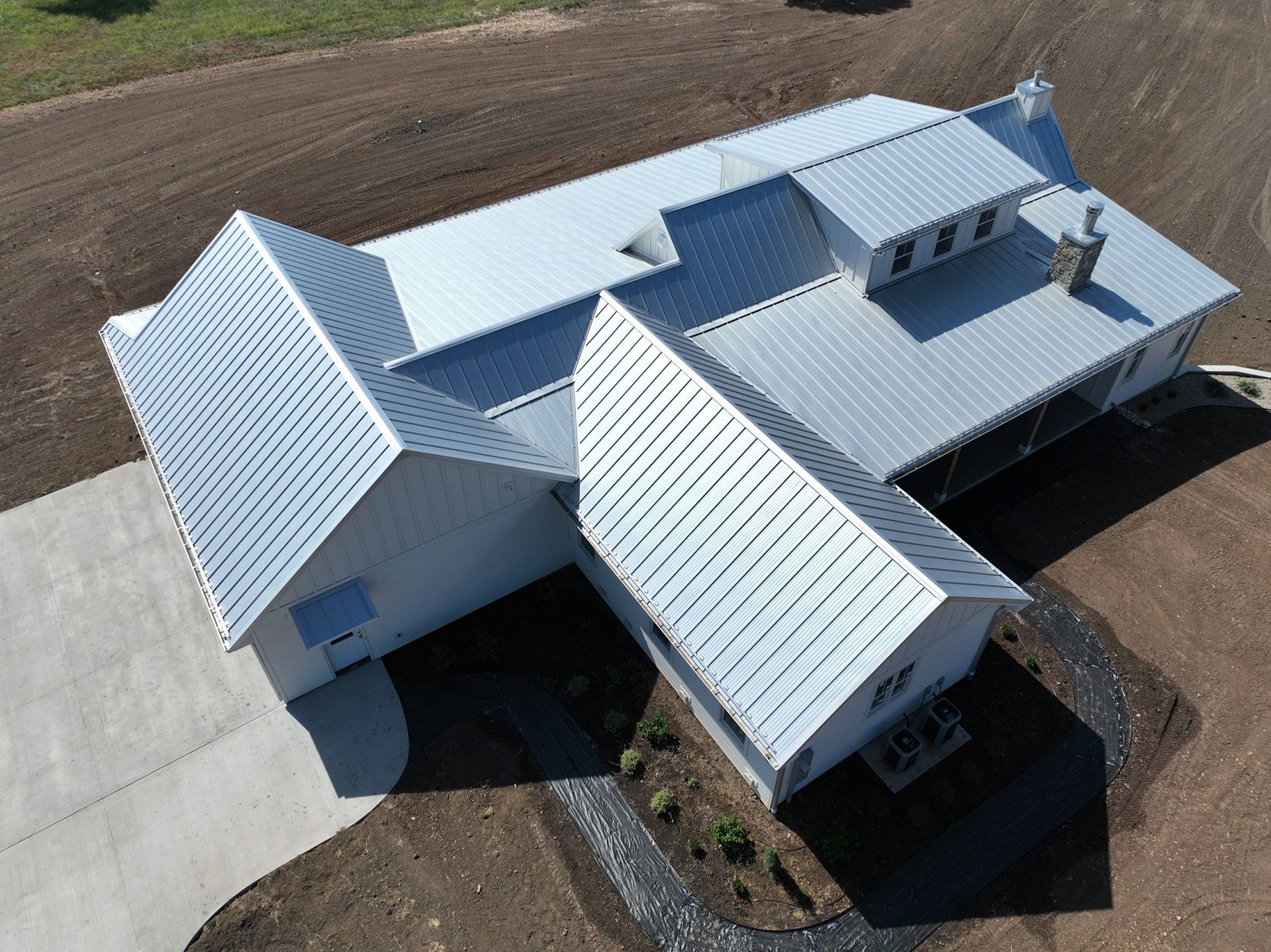 Aerial view of a white house with a corrugated metal roof and a concrete driveway.