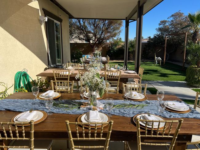 Set dining table on a patio with gold chairs, white plates, and floral centerpieces