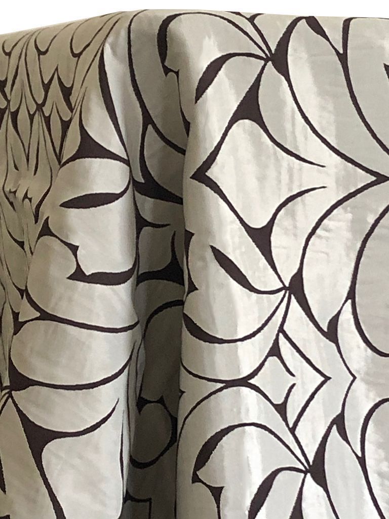 Close-up of fabric. Pale silvery background with dark brown stylized floral pattern.