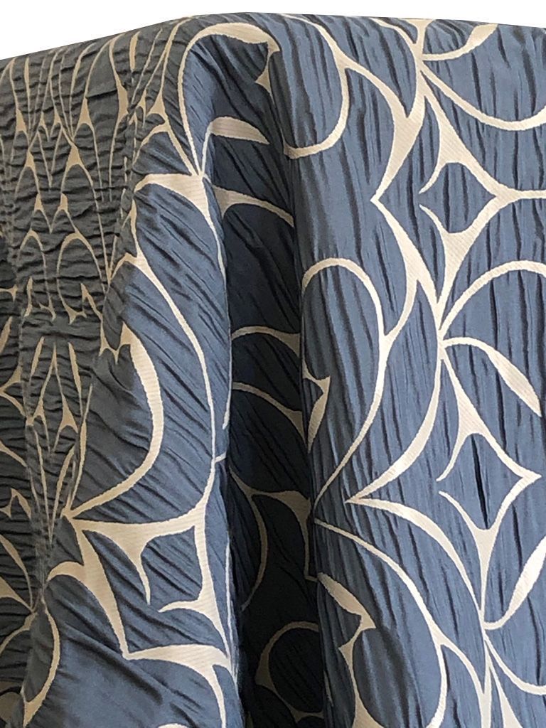 Blue fabric with white abstract floral pattern, textured and draped.