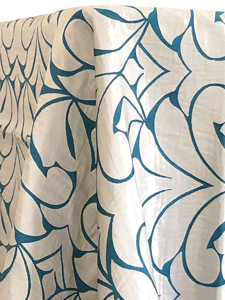 White fabric with teal floral pattern, hanging and folded.