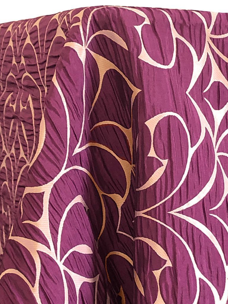 Purple fabric with a textured surface and a cream-colored floral pattern.