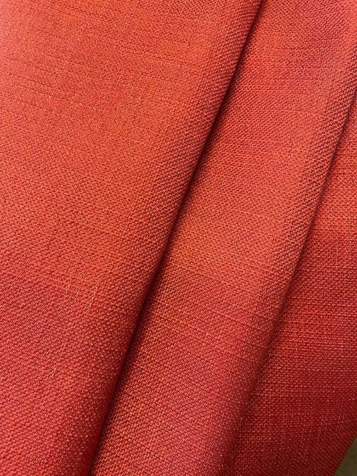 Close-up of orange-red fabric with woven texture, folded in diagonal lines.