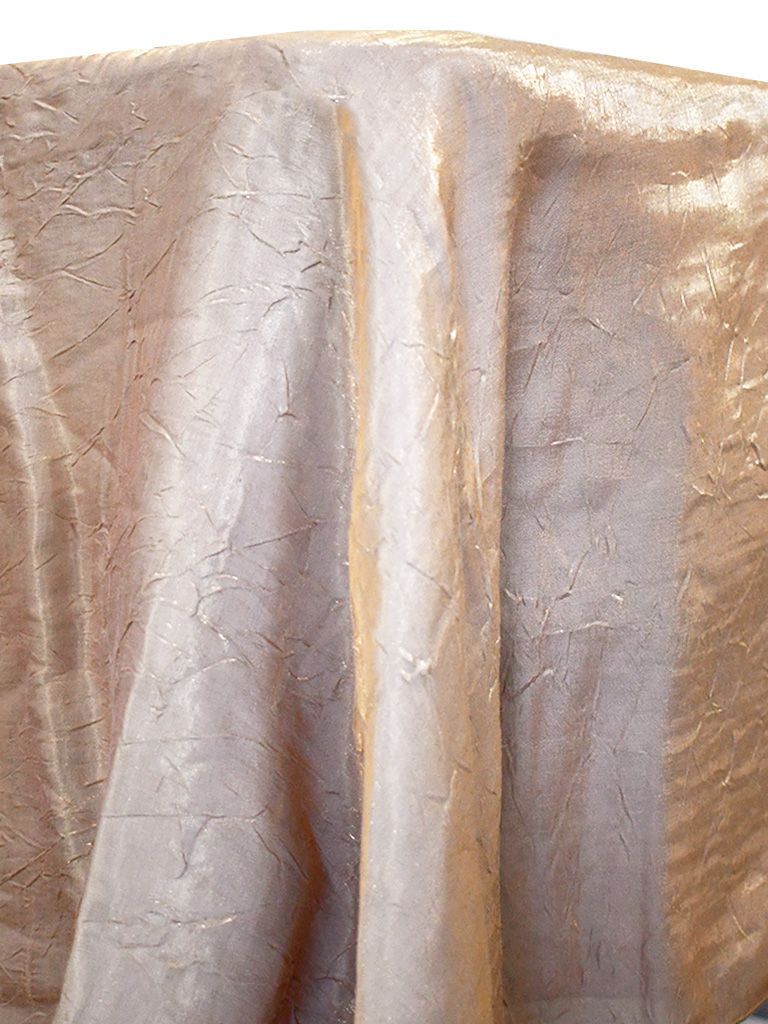 Tan, shimmery fabric draped over a surface, with vertical folds and subtle texture.