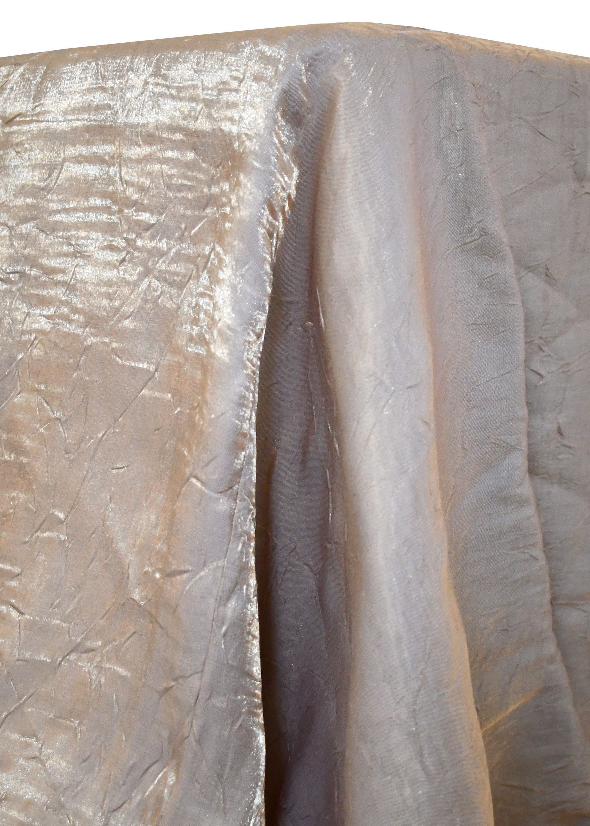 Beige, shimmery fabric draped over a surface, with folds and texture visible.
