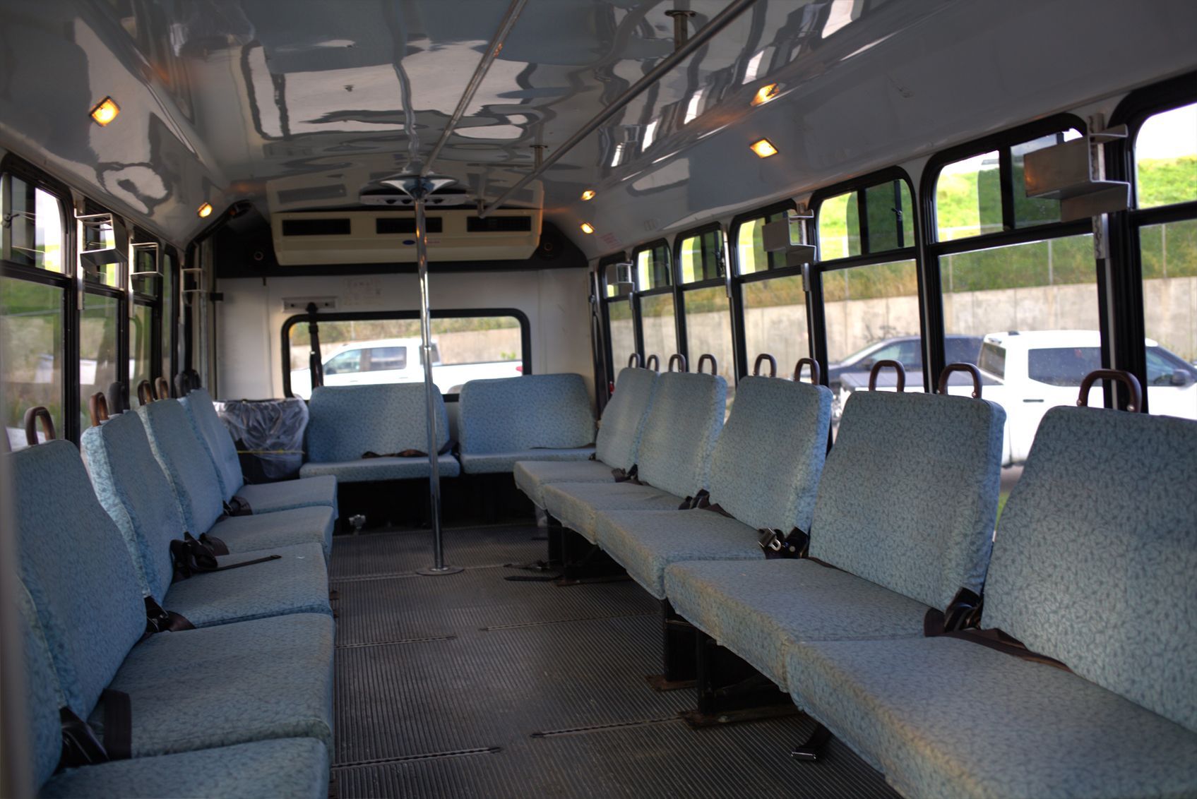 Interior of a bus with rows of blue seats, windows, and a center pole.