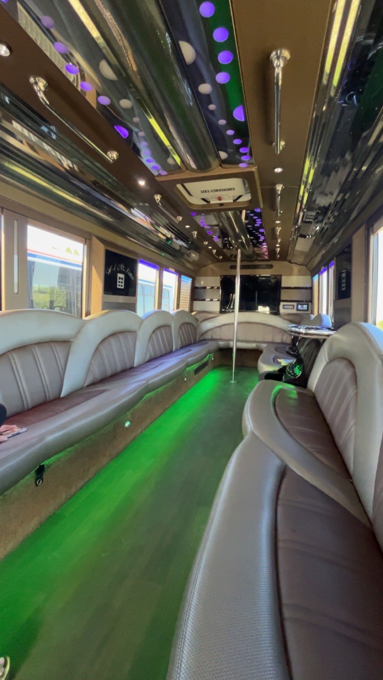 Interior of a luxury party bus with leather seating, green floor lights, mirrored ceiling, and a central pole.