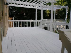White wooden deck with railings and pergola, overlooking a wooded yard.