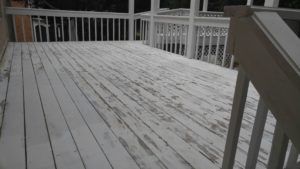 Snow-dusted wooden deck with white railings and stairs at right, viewed from inside a house