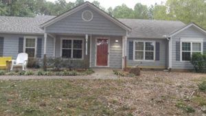 Single-story gray house with a red front door and a large yard in front.
