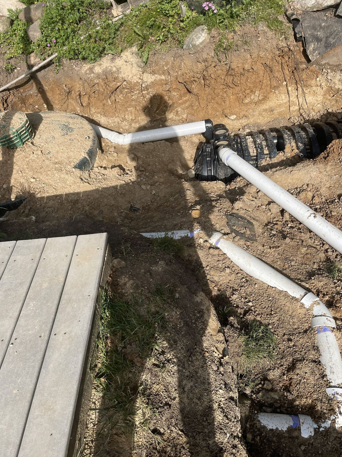 Pipes and a drainage system in a dirt trench next to a concrete walkway