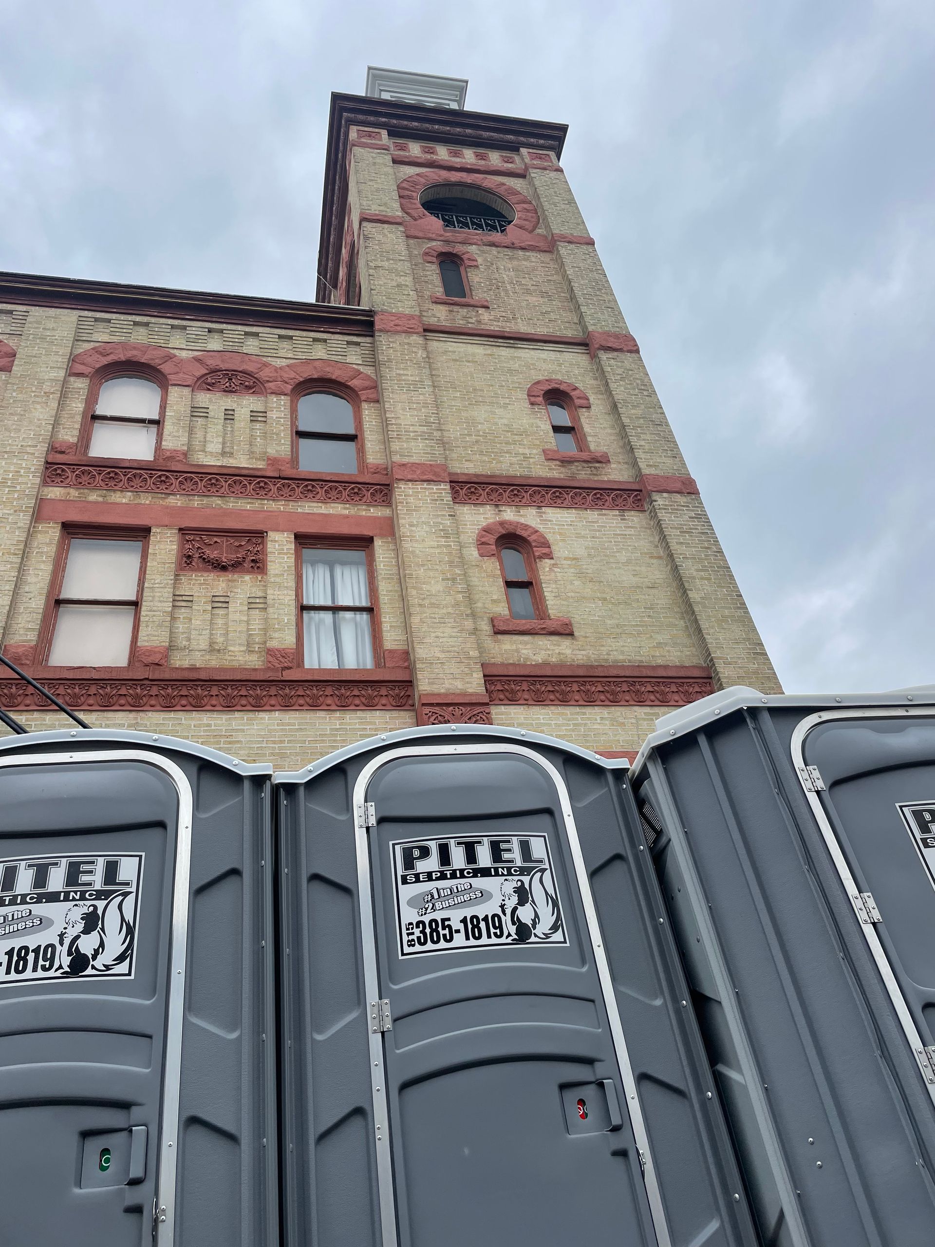 Tall brick building with clock tower, gray portable toilets in foreground