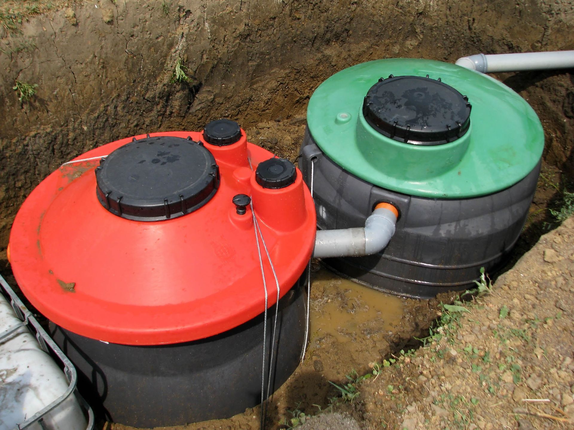 Two buried septic tanks, one red-topped, one green-topped, connected by a pipe.