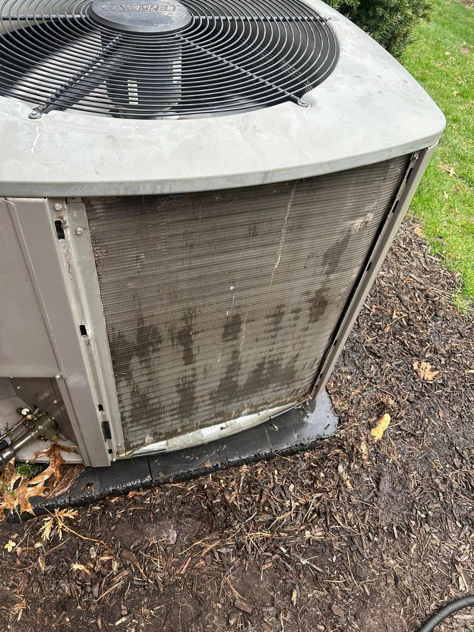 Outdoor AC unit with dirty, clogged coils, gray metal, and a fan at the top. Set on a concrete pad.