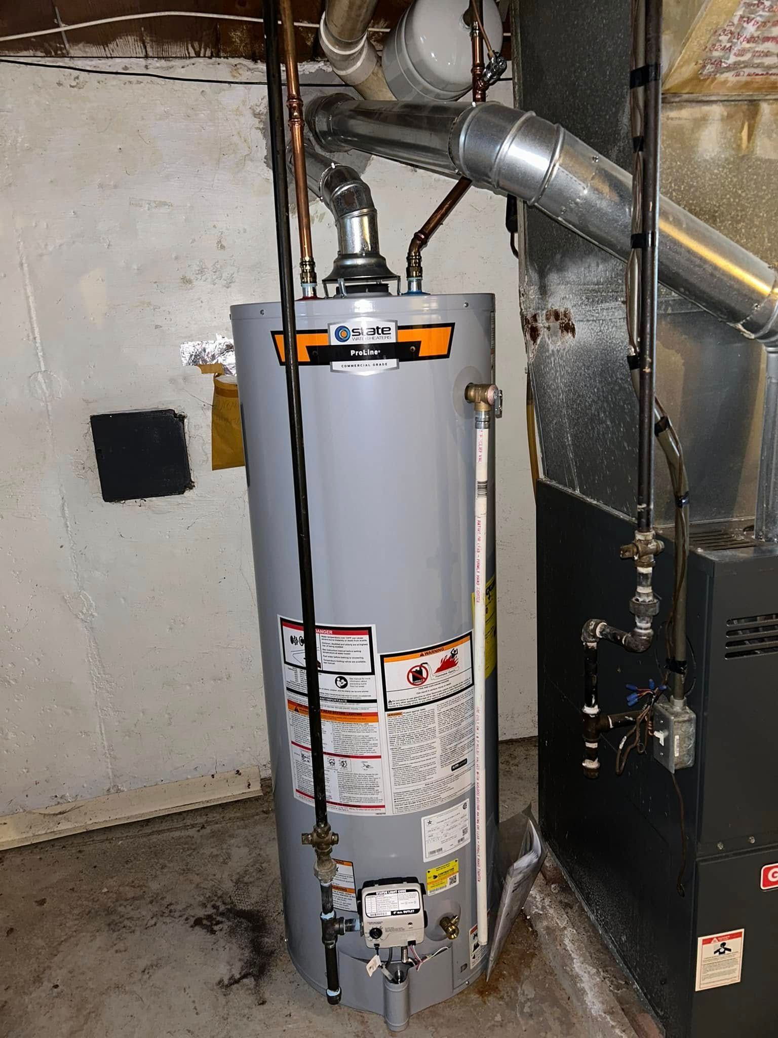 A water heater in a basement setting, next to a furnace. Gray and silver with connected pipes.