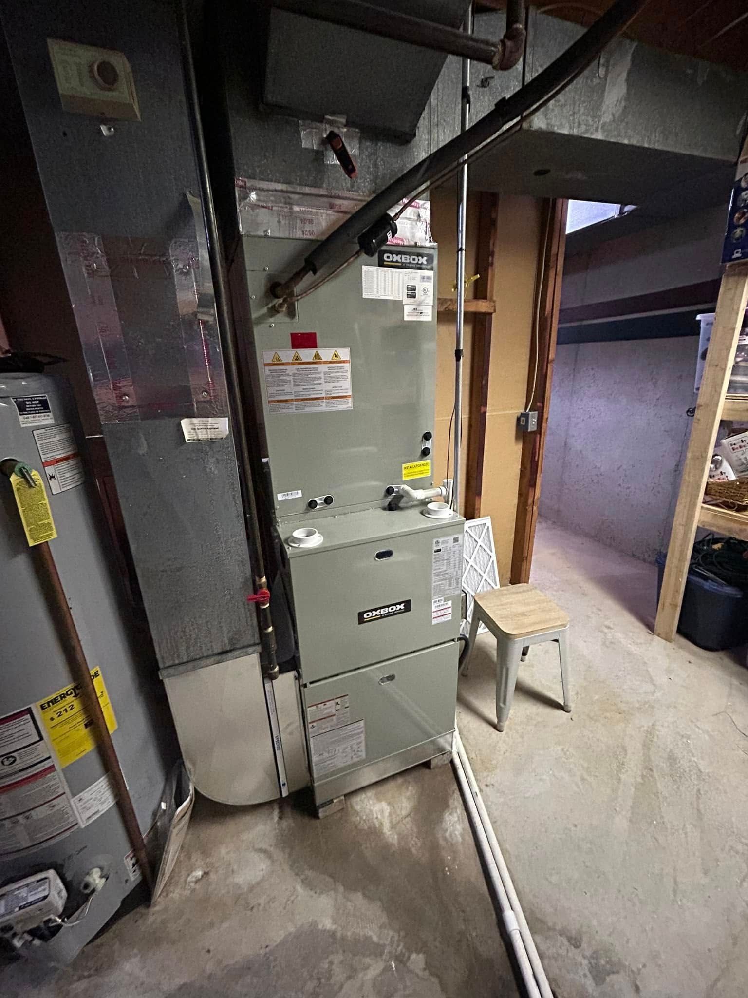 Furnace and air conditioning unit in a basement. Gray metal appliances. White pvc pipe.