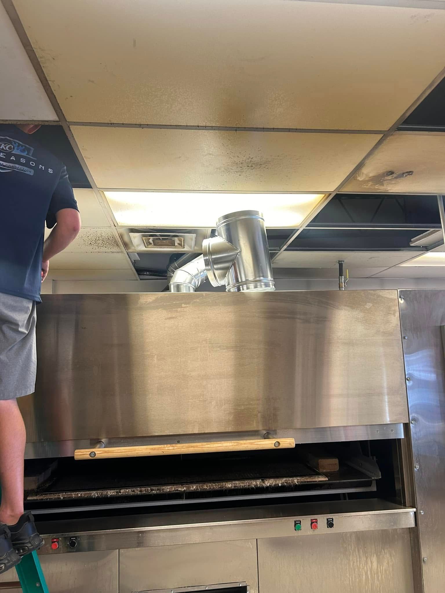 Man on ladder installing kitchen exhaust hood in a restaurant. Damaged ceiling tiles.