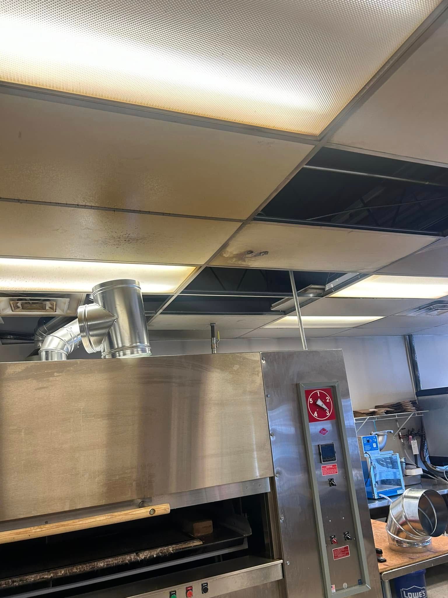 Stainless steel pizza oven in a commercial kitchen, with a vent and control panel visible.