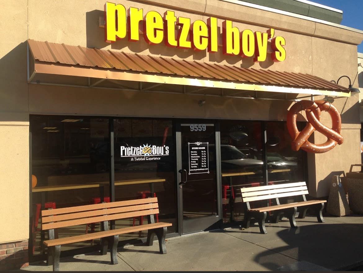 Pretzel Boy's storefront with brown awning, yellow sign, benches, and a pretzel-shaped sign.